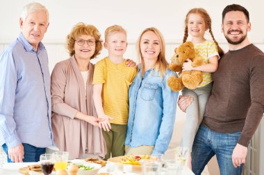 Portrait of happy two generation family of six posing at home smiling happily looking at camera standing at festive dinner table clipart