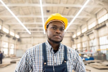 Kask ve müzik kulaklık duran geniş üretim bölümü modern bitki genel dinlemek yakışıklı Afro-Amerikan makine operatörünün portre çekim.