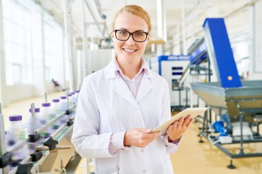 Çekici genç Müfettiş duran geniş Soya süt fabrikası ile dijital tablet bel-up portre vurdu ellerinize, çekici gülümseme ile kameraya bakarak beyaz önlük giyiyor