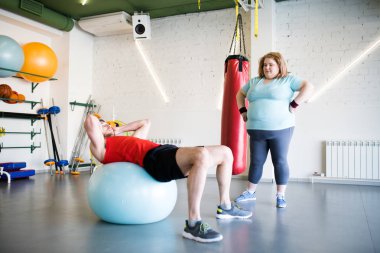 Spor salonunda fitness Ball Egzersizler yapan obez genç kadın izlerken yakışıklı erkek portresi tam uzunlukta