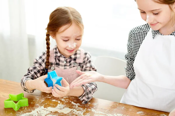 Cute little girl passing cookie cutter to elder sister while preparing delicious present for Mothers Day, close-up shot