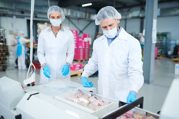 包装用フィルムに菓子紙箱をラップする機械を使用して白衣の製菓工場労働者 — ストック写真