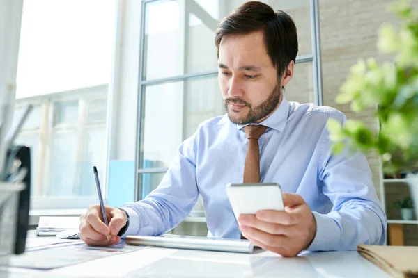 Elegante Hombre Barbudo Usando Smartphone Tomando Notas Papel Trabajando Mesa — Foto de Stock