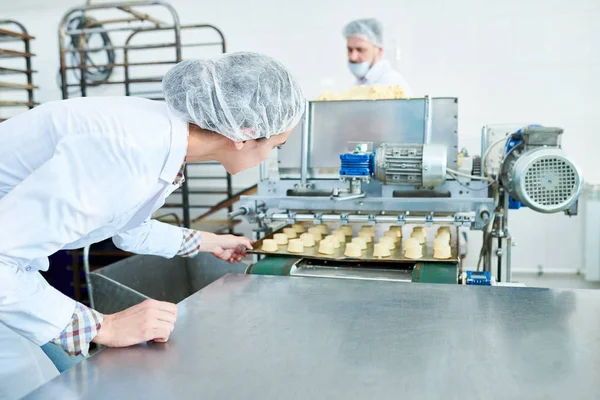 ヘアネット調理菓子とベーキング シートを押しながら機械に製菓工場従業員 — ストック写真