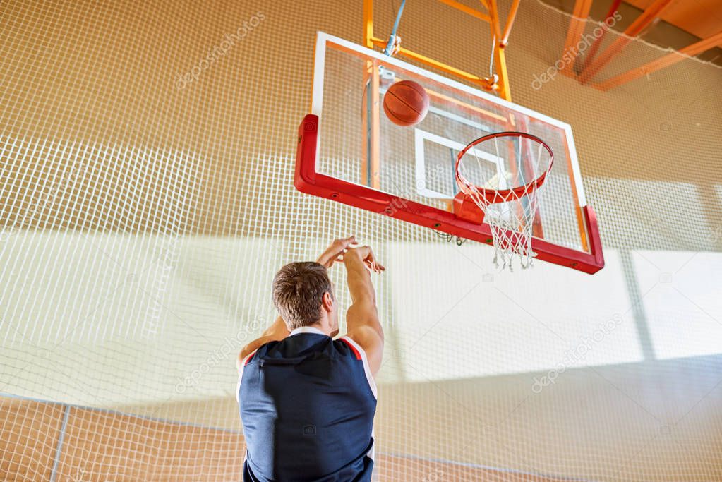 Back view of faceless man in basketball uniform shooting goal while playing in gym. 