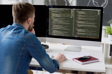 Dikiz konsantre düşünceli erkek programcı yeni modern office programında çalışırken bilgisayar monitöründe bilgisayar dili kod görüntüleme