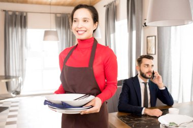 Neşeli pozitif genç karışık yarış garson önlük yemekten, kendine güvenen adam arka planda telefonda konuşurken sonra bulaşık işadamı tablo taşıma