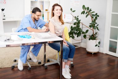 Tam uzunlukta stetoskop kullanarak ve nefes neşeyle Danışma modern klinik süreci sırasında gülümseyen güzel genç kadın için dinleme genç Orta Doğulu Doktor portresi