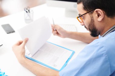 Office ve okuma hastalar raporlarındaki masada oturan gözlüklü genç Orta Doğulu Doktor portresi yüksek açı