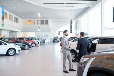 Profesyonel satış temsilcisi bir modern otomatik salonda yeni araba satıyorsun. İki adam ayakta ve yeni bir araba seçimi