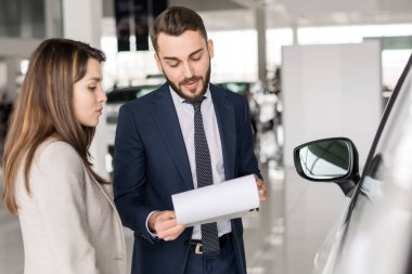 Bel kadar yakışıklı araba satıcısı ona araba showroom seçmenize yardımcı genç bir kadın konuşmaya portresi
