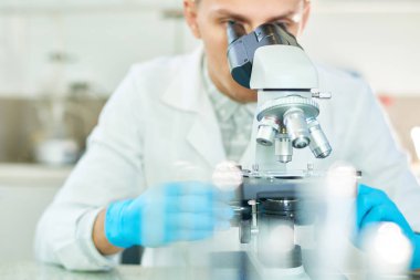 Lastik eldiven ve modern laboratuarındaki yapay et oluşturulması üzerinde çalışırken mikroskop seyir beyaz önlük giyen çalışkan genç bilim adamı