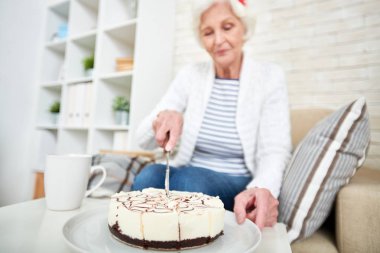 Çay doğumgününde yalnız evde içmek üzere hazırlanırken bıçakla sakin güzel yaşlı kadın kesme pasta