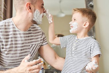 Sevimli küçük çocuk birlikte banyoya eğlenirken sevgi dolu babası yüzünde traş köpüğü uygulama