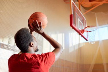 Anonim Afrikalı-Amerikalı sporcu spor salonunda basketbol oynarken hedefi vurmaya hazırlanıyor.