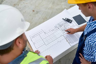 Kat planları tartışmak ve sitede belgelere mühendislik iki inşaat işçileri, yüksek açılı görünüş