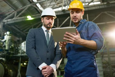 Genç fabrika işçisi bir şey modern tesisi, kopya alanı atölyede kask giyen işadamı için gösterilen dijital tablet kullanarak portresi