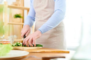 Tanınmayan Cook geniş stüdyoda ayakta ve Mutfak Atölyesi iletken önlük kesim salatalık giyen yakın çekim shot