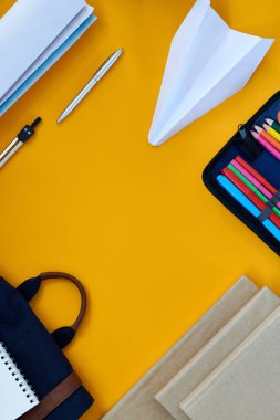 Üstten görünüm flatlay kompozisyon kağıt uçak üstünde okul sırası, kopya alanı ve yaşam tarzı kalemlerde sarı arka plan, sharpies planlayıcısı
