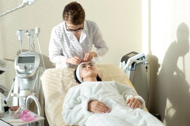 Tedavi masada duran ve yordam, başlamadan önce gerekli hazırlıkları arka plan üzerinde modern yüz odanın iç yapım beyaz önlük giyen son derece profesyonel güzellik uzmanı