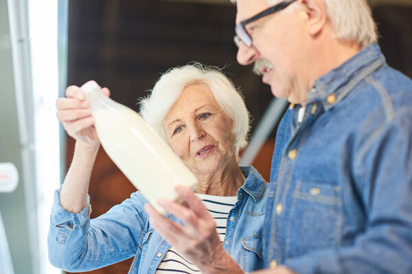 Portrait of modern senior couple choosing milk standing by dairy isle in supermarket while grocery shopping