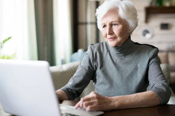 テーブルに座って ノート パソコンを見ての白髪の魅力的な年配の女性 — ストック写真