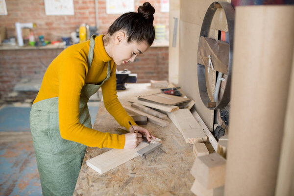 Side view portrait of young female artisan working with wood in modern carpenters manufactory