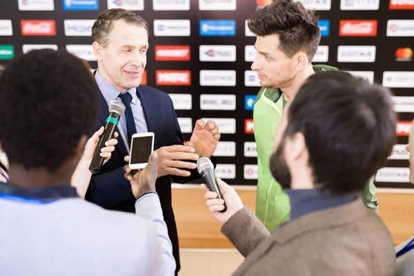 Portrait of young professional sportsman and his mature manager answering questions of journalists during press conference