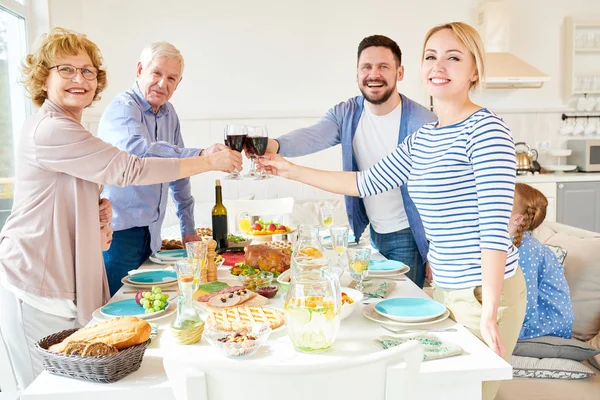 Portrait of happy two generation  family enjoying dinner together clinking glasses over festive table  with delicious dishes and smiling looking at camera, copy space
