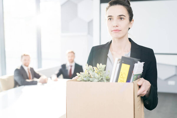 Waist up portrait of young businesswoman holding box of personal belongings  leaving office after quitting job