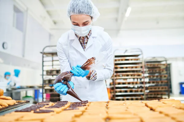 菓子の袋からチョコレート クリームを絞り白衣の製菓工場従業員 — ストック写真