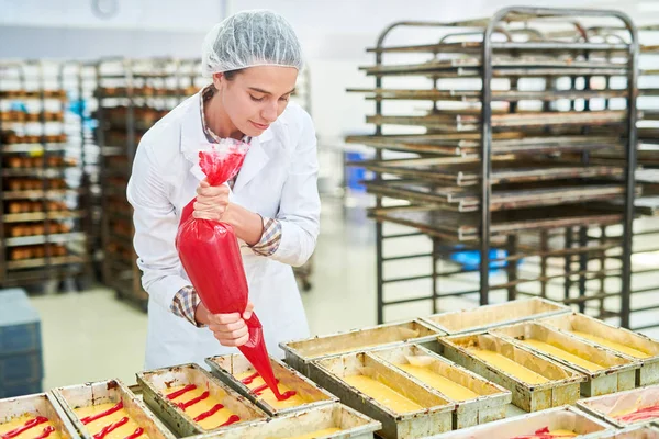 菓子の袋から白いコート注ぐ赤クリームの菓子工場労働者 — ストック写真