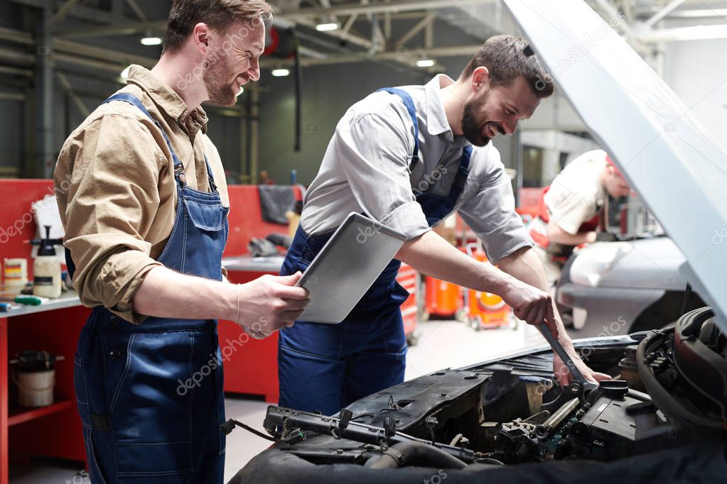 Portrait handsome of two workers fixing car in service workshop and smiling happily