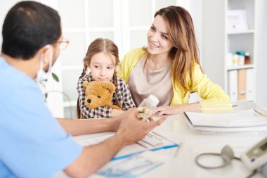 Güzel genç anne doktor ofisinde masada oturan ve çocuk için doktoru ziyaret sırasında dinleme sevimli küçük kız portresi