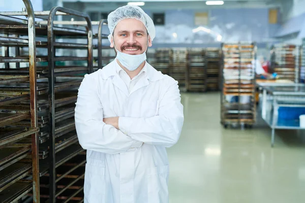 Confectionery factory worker standing in white coat with arms crossed smiling and looking at camera.