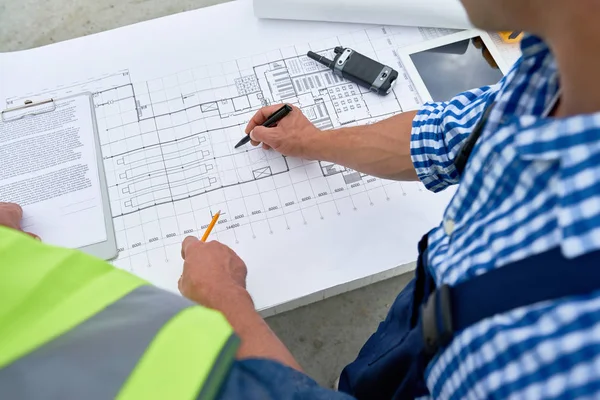 High angle close up of two construction workers looking at floor plans and engineering documentation on site