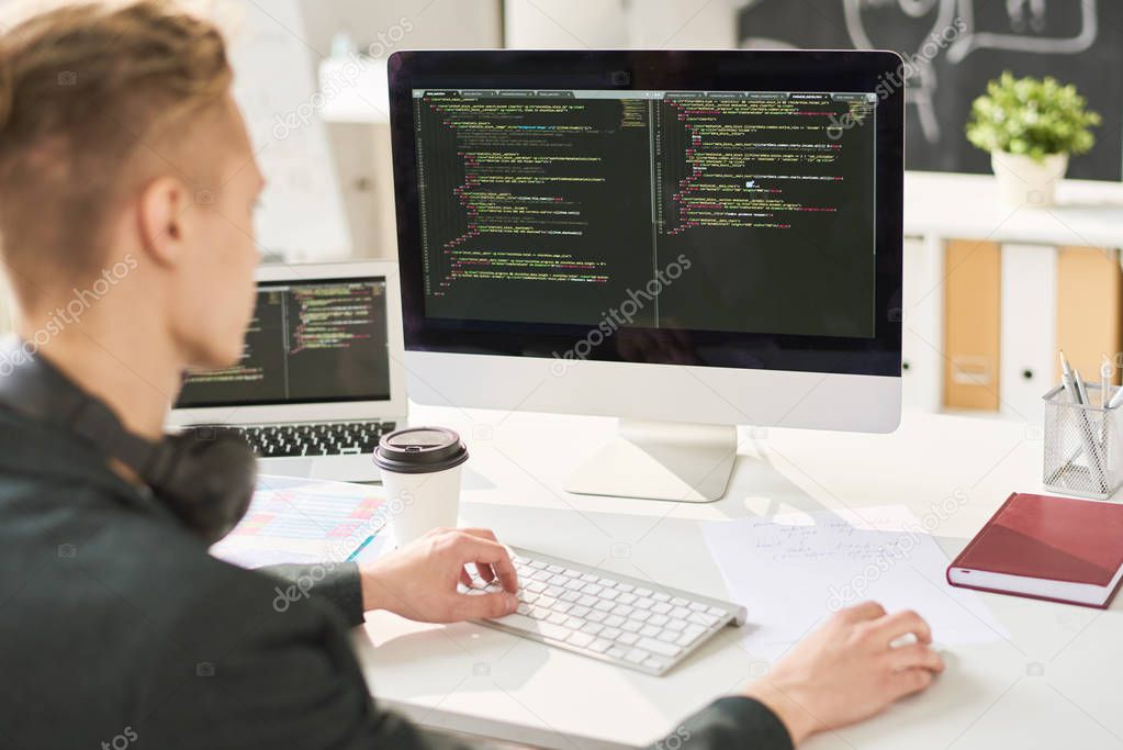 Busy smart web developer editing computer programming code and sitting at table in modern office