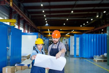 Atölyede üretim tartışırken planları tutan hardhatlar giyen iki modern fabrika işçisinin bel kadar portre, kopyalama alanı