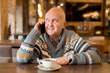 Kahve dükkanında arkadaş beklerken olumlu içerik yakışıklı olgun adam kahve fincanı ile masada oturan ve cep telefonu ile konuşurken