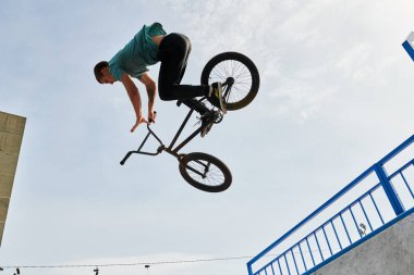 Genç adam BMX stunts aşırı spor parkında rampa üzerinde gökyüzüne karşı yüksek atlama yapıyor yan görünüm portre, kopya alanı