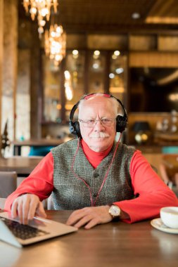 Bıyıklı ciddi üst düzey adam masada oturan şık bir kıyafet giyiyor ve kameraya bakarak, o kulaklık ile müzik dinlerken ve dizüstü bilgisayar kullanarak