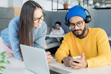 Video izlerken ve çalışma alanında yeni proje hakkında fikirler paylaşan akıllı telefon kullanarak Casual giyim içerik yaratıcı genç çalışanlar