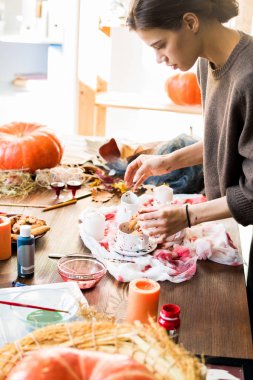 Ahşap masada duran ve çekim için Halloween dekorasyon yerleştirme seçimi kahverengi kazak Ciddi yaratıcı kadın tasarımcı, o kanlı lekeler ile fincan cadı parmak çerez koyarak