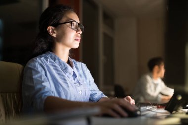 Karanlık ofiste gece geç saatlerde bilgisayar kullanırken yazma Karışık ırk genç kadın düşük açılı portre