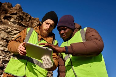 Biri Afrikalı, iş yerinde ki maden madenlerini denetleyen ve dijital tablet kullanan, kopya alanı olan yansıtıcı ceketler giyen iki sanayi işçisinin düşük açılı portresi