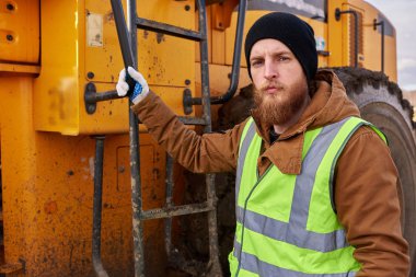 Ağır sarı kamyon la poz veren ve kameraya bakan sakallı işçinin bel den yukarı portresi, kopya alanı