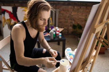 Dim sanat stüdyosunda şelat la çalışırken suluboya boyaları karıştıran çağdaş uzun saçlı sanatçının portresi