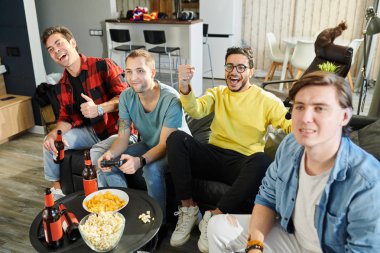 Arkadaşlarıyla video oyunu oynayan iki adam onlara tezahürat yapıyor ve bira içiyor.