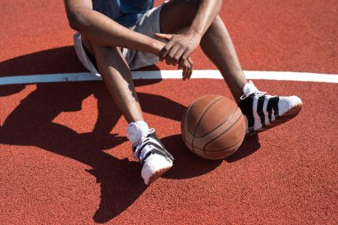 Ön planda topu ile açık mahkeme katta oturan tanınmaz Afrika basketbol oyuncusu düşük kesit portre, kopya alanı