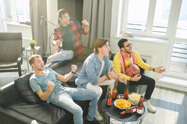 Genç erkekler kanepede oturup, bira içip, evde televizyon seyrediyorlar.